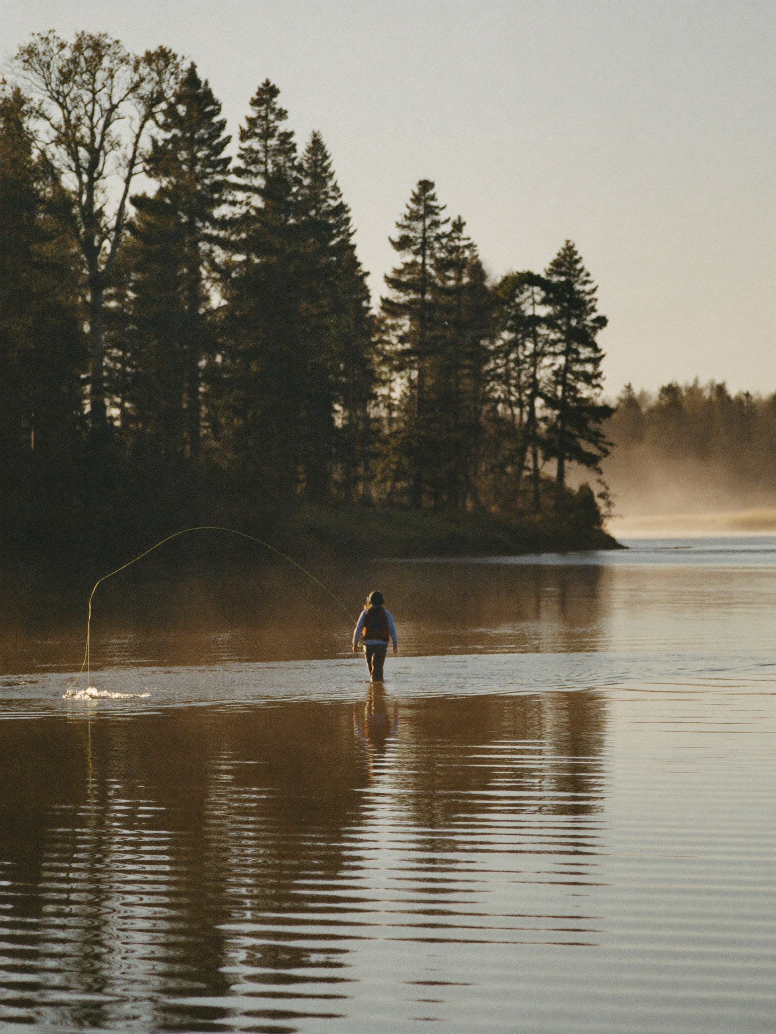 Fly fisherman casting mid-river at golden hour