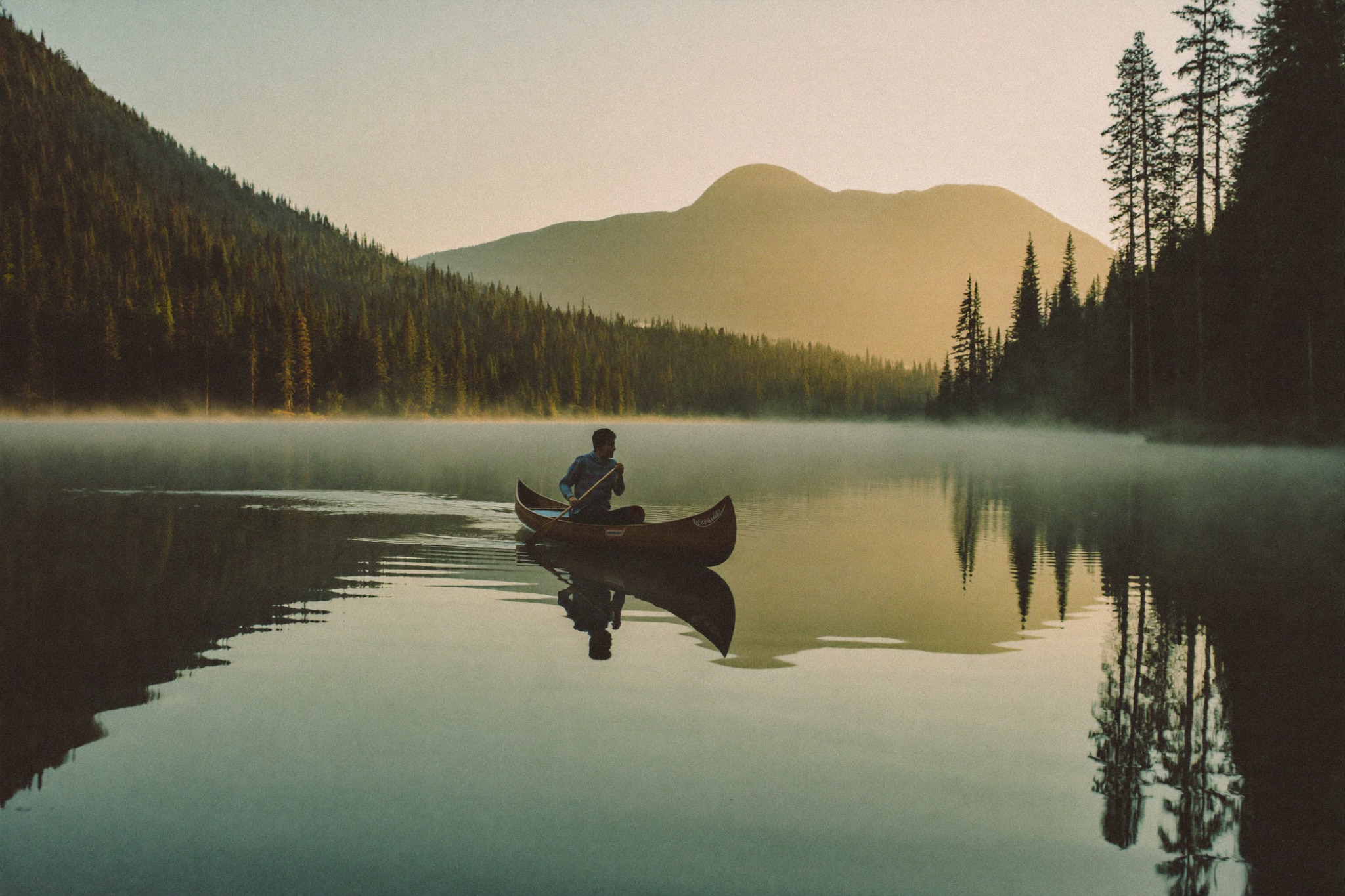 Canoe crossing a still, misty lake at sunrise